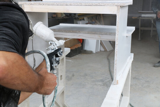 Worker painting wooden product with spray gun in carpentry's painting workshop. occupational safety