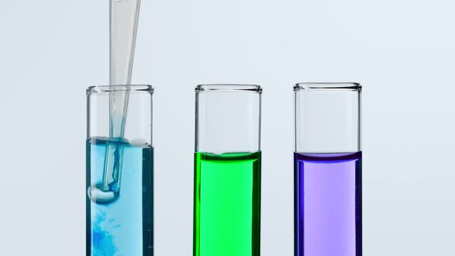 Concept of science and biotechnology. Closeup of laboratory utensils on white background. Test tubes filled with purple, green, blue liquid, scientist pipetting blue liquid from test tube. Slow motion