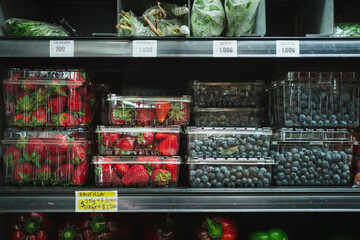 Strawberries and blueberries in plastic boxes at fridge shelf in fruit store in Chile