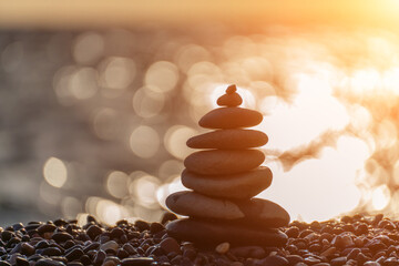 Balanced rock pyramid on pebbles beach. Golden sea bokeh on background. Selective focus, zen stones...