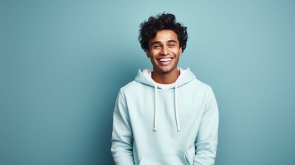 People lifestyle concept. Studio shot of young happy smiling Hindu male student standing isolated in centre on blue background wearing casual hoodie and jeans with white leather bag