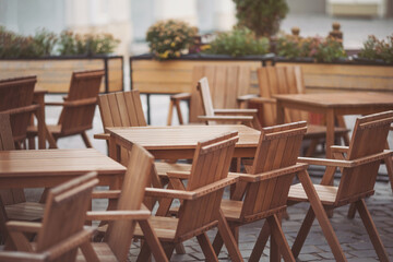 Fototapeta na wymiar Wooden chairs and tables. Outdoor terrace concept. Copy space. Old fashioned empty cafe terrace with vintage chairs and tables. Loft style cafe. Empty restaurant summer terrace. Street view