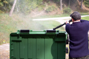 A municipal service worker treats a garbage container with a disinfectant solution. Washing the garbage container.	