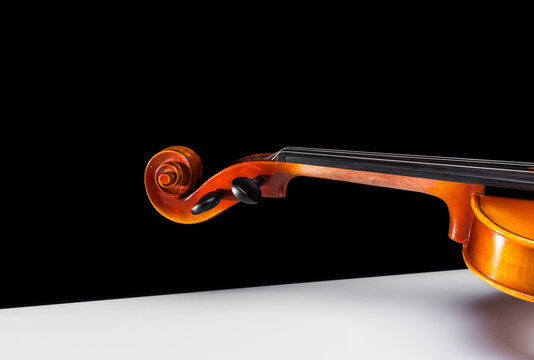 Scroll neck and and fingerboard of a violin seen from the side on a white background isolated against a black background