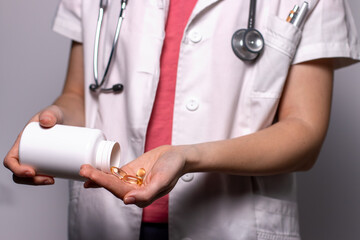 Woman doctor nutritionist hands in white shirt with omega 3, vitamin D capsules. The doctor spills...