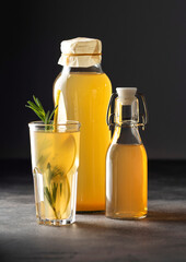 Pear kombucha with rosemary in a glass and bottles on a dark background, vertical orientation, close-up
