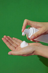 Hand pressing on a jar of cleansing foam, mousse contained in a white plastic pump jar on green background. Skin care concept, banner, mock up, template. Daily hygiene, caring for face, body. Close up