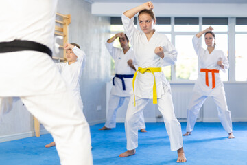 Teen girl and her family during practice of karate kata standing in row and closely watching man...