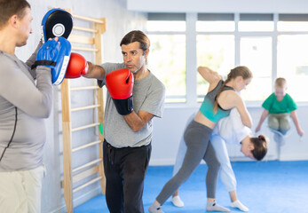 Man trains to deliver strong and fast blow to boxing paws during boxing training session. Rehearsal...