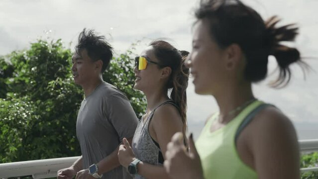 side view of three happy young asian people jogging running exercising outdoors in park