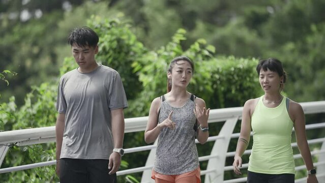 three happy young asian people walking relaxing chatting talking while exercising outdoors in park