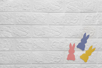 Three colored paper rabbits on white brick wall. Place for text. Paper cut bunnies on white...