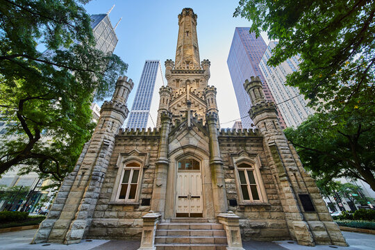 Chicago Water Tower front entrance with lit tower and bright skyscrapers behind framed by lush trees