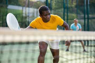Athletic african american man plays padel. View through tennis net