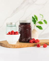 Homemade raspberry jam on kitchen counter with fresh raspberries