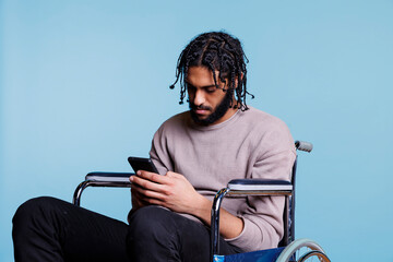Arab man sitting in wheelchair while scrolling social media on smartphone. Young person with...