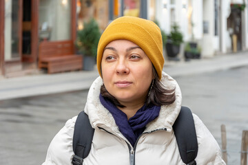 Street portrait of a pensive woman wearing a yellow hat against a blurred winter urban European background.