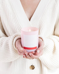Woman holding lit pink candle with hand in front of her 