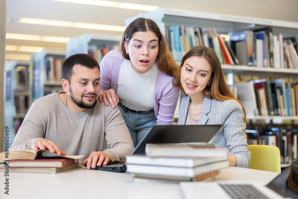 Canvas Prints Group of enthusiastic young adult female and male colleagues working together in public library, discussing while sitting at table with laptop and books..