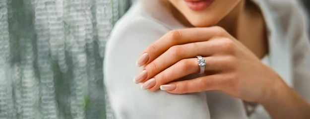 Fotobehang Woman Flaunting Her Elegant Diamond Engagement Ring. Close-up of a woman's hand as she shows off a sparkling diamond ring, symbolizing engagement © Igor Tichonow