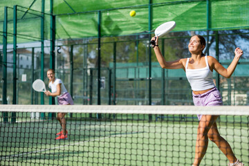 Two active women tennis players, playing padel on an outdoor court, using rackets to hit the ball