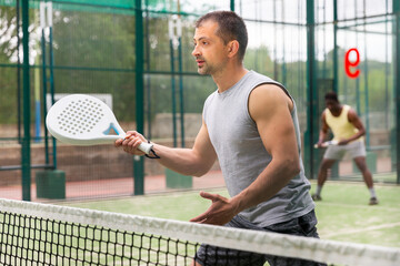 Portrait of man playing with male partner padel doubles game on outdoors court