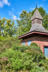 Fototapeta premium Charming Brick Garden Shed with Weathervane and Lush Foliage