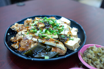 Chinese food, fried tofu with soy sauce on black plate on wooden table
