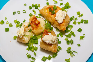 Fried pieroguis Ukrainian traditional food, on white plate on tablecloth decorated with typical Ukrainian embroidery. With cream and fresh chives in fine details. Prudentópolis PR