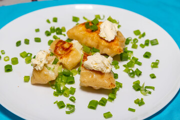 Fried pieroguis Ukrainian traditional food, on white plate on tablecloth decorated with typical Ukrainian embroidery. With cream and fresh chives in fine details. Prudentópolis PR