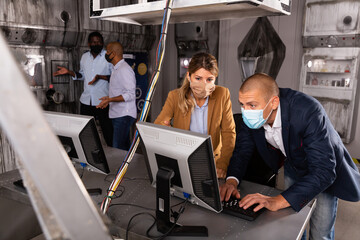 Man and woman in protective masks in panic looking for a solution on the computer in the quest room