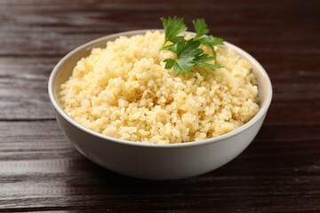 Delicious bulgur with parsley in bowl on wooden table, closeup