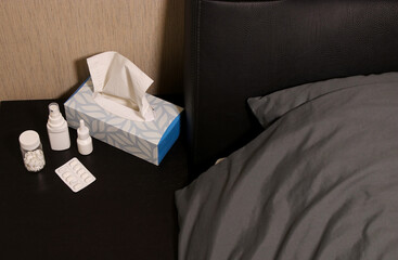 Headache pills, nose spray, throat spray and tissue box on a night table near bed