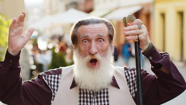 Oh my God, Wow. Bearded senior man looking surprised at camera with big open eyes shocked by sudden victory game winning lottery goal achievement good news outdoors. Elderly grandfather in city street