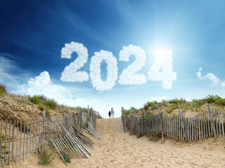 Happy new year 2024! Two kids on the beach in front of 2023 shaped clouds.