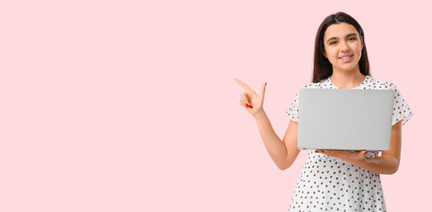 Young woman with laptop showing something on pink background with space for text