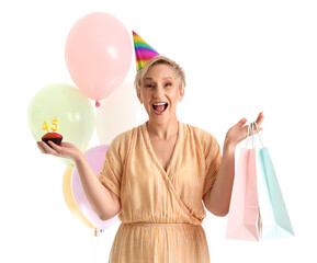 Happy mature woman with birthday muffin and bags on white background