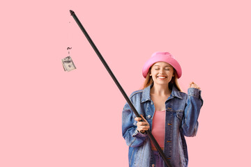 Happy young woman with fishing rod and money on pink background