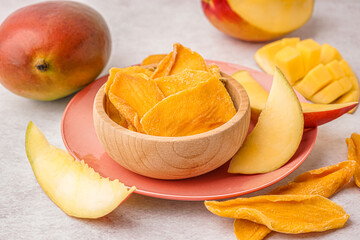Wooden bowl with slices of dried mango on white table
