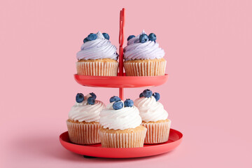 Dessert stand of tasty cupcakes with blueberries on pink background