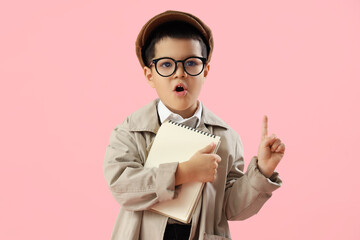Shocked little detective with notebook pointing at something on pink background