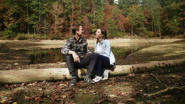 Couple Sit and Talk on Log next to Mountain Lake
