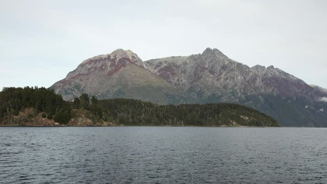 A boat navigating the lake in the morning. View of the forest and rocky mountains.
