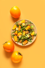 Plate of delicious salad with persimmon, pomegranate seeds and walnut on orange background