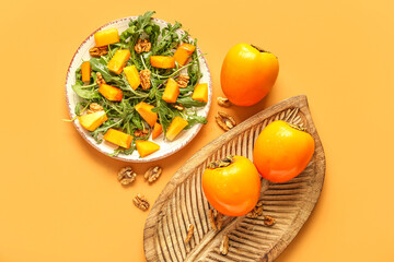 Plate of delicious salad with persimmon and walnut on orange background