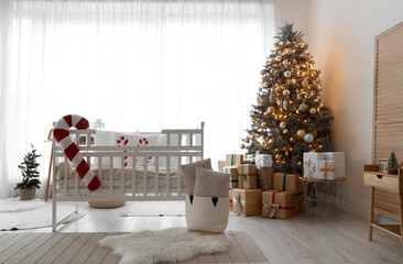 Interior of light bedroom with baby crib, Christmas tree and presents