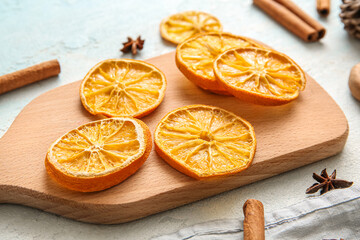 Wooden board with dried orange slices and cinnamon on light blue background