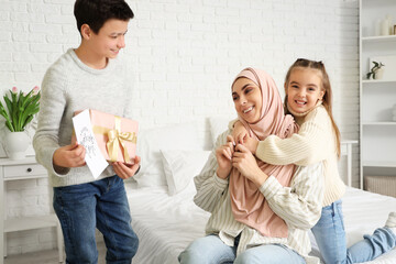 Little children greeting their Muslim mother with gifts in bedroom