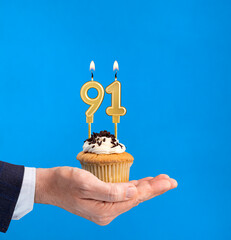 Hand holding a cupcake with the number 91 candle - Birthday on blue background