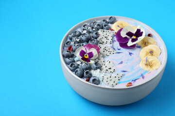 Obraz na płótnie Canvas Delicious smoothie bowl with fresh fruits, blueberries and flowers on light blue background, closeup. Space for text